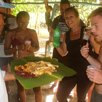 Travelers and locals sharing a joyful moment around a plate of Dominican specialties served on banana leaves
