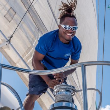 Crew member smiling at the helm while sailing on the Quetzal catamaran