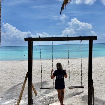 Traveler enjoying a swing on a white sandy beach with turquoise sea view during Saona excursion