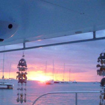 Sunset view from the deck of the Quetzal catamaran, with hanging seashell decorations and boats in the distance